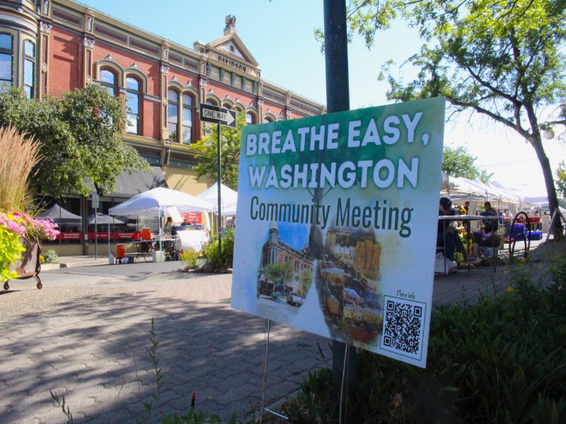 A sign at a street fair advertises a community meeting about air quality