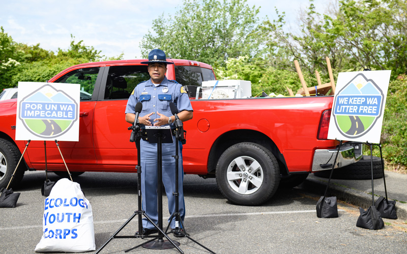 A police officer standing with signs and vehicle in background.
