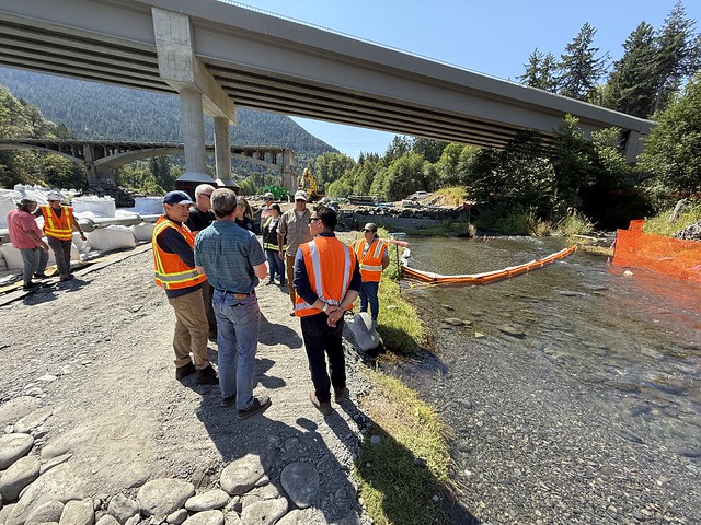 People from Ecology, Unified Command, and the Lower Elwha Klallam Tribe stand near Indian Creek and wear orange emergency vests. 