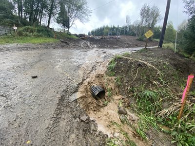 Excessive muddy water flows off a construction site, over a damaged road.