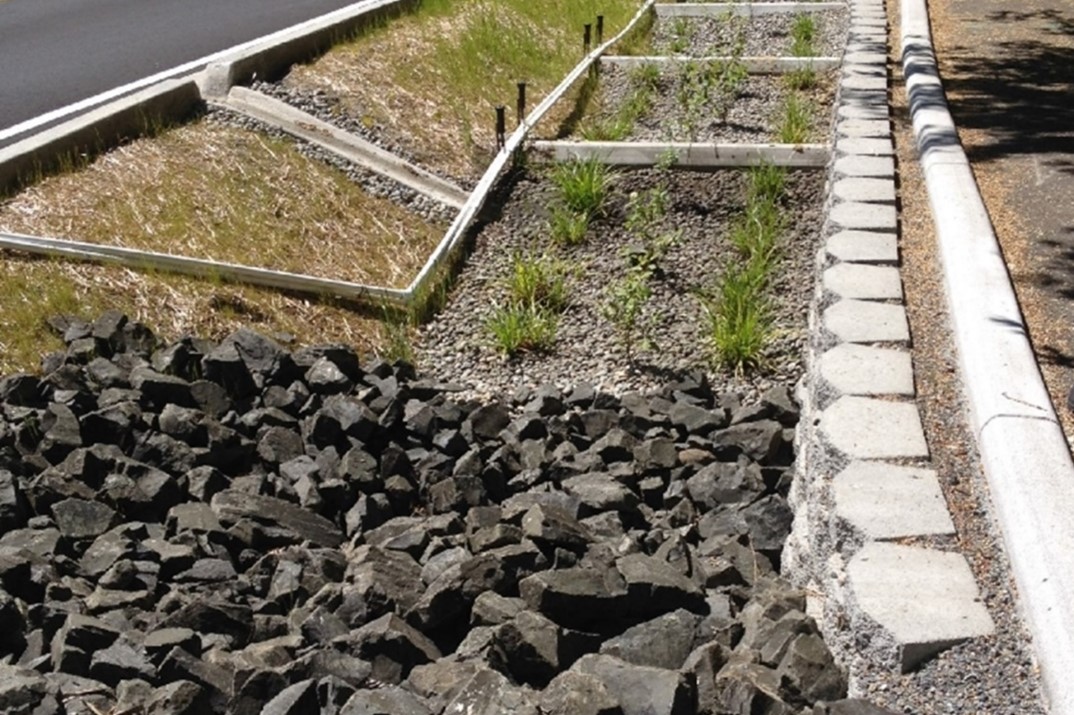 drains from the road leading to side area with plants, rocks, and gravel to slow stormwater