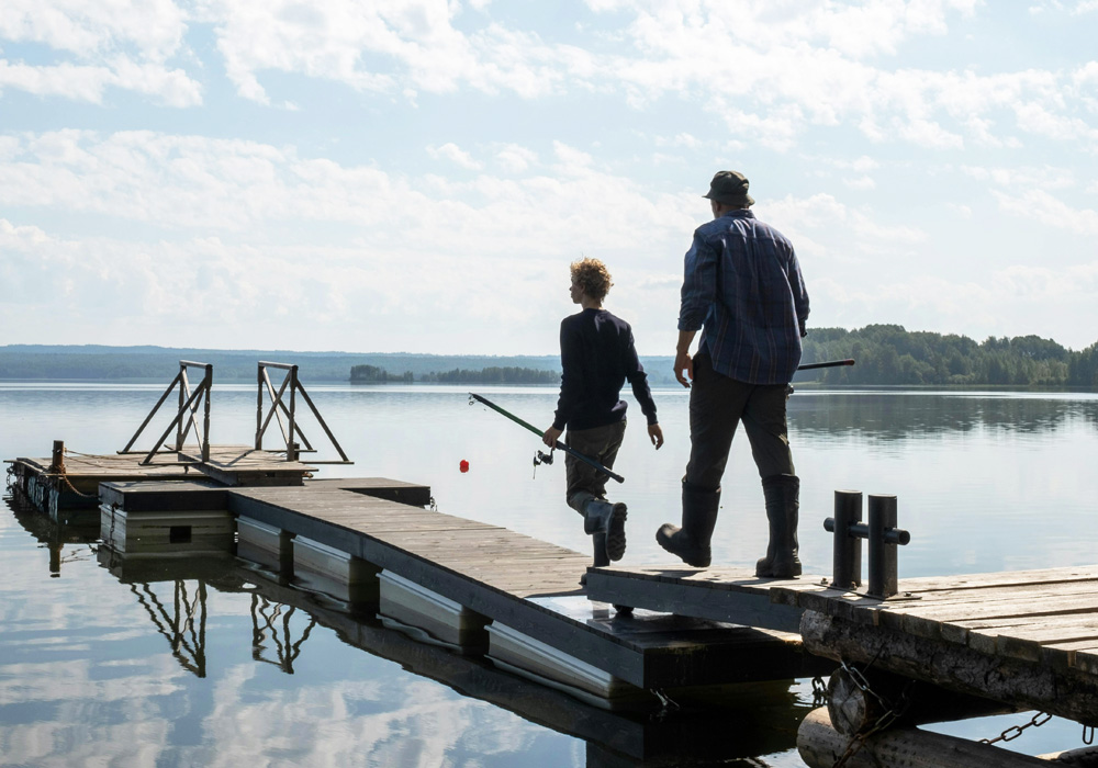 Two people walking on a fishing dock with fishing poles in the hands.