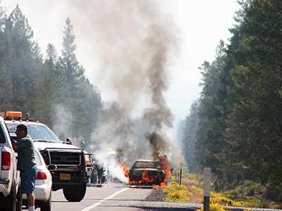 car on fire on side of road near forest