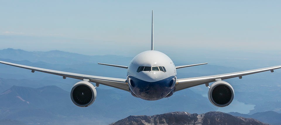 a commercial jet airplane flying over a mountainous area and a river.