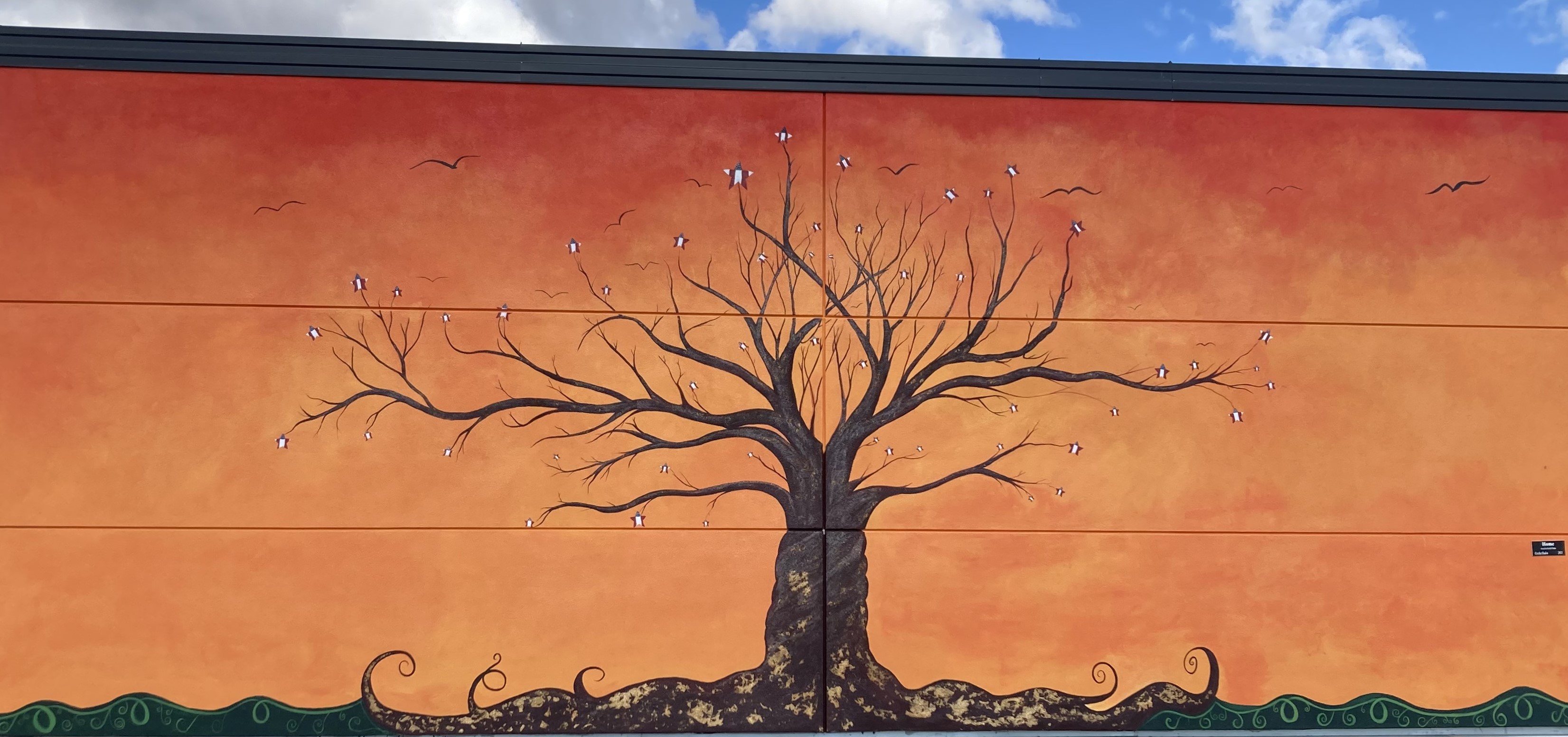Mural of a stylized tree stretching over a sunset-orange sky.