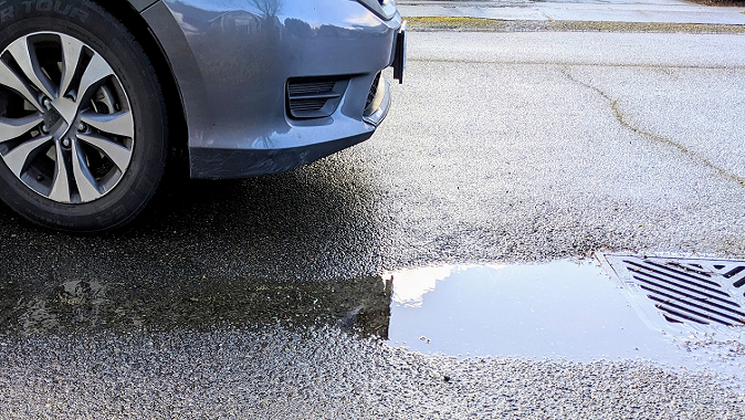 front of car showing tire and standing water on street near stormdrain