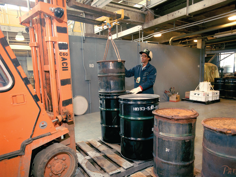Workers move drums with a forklift.