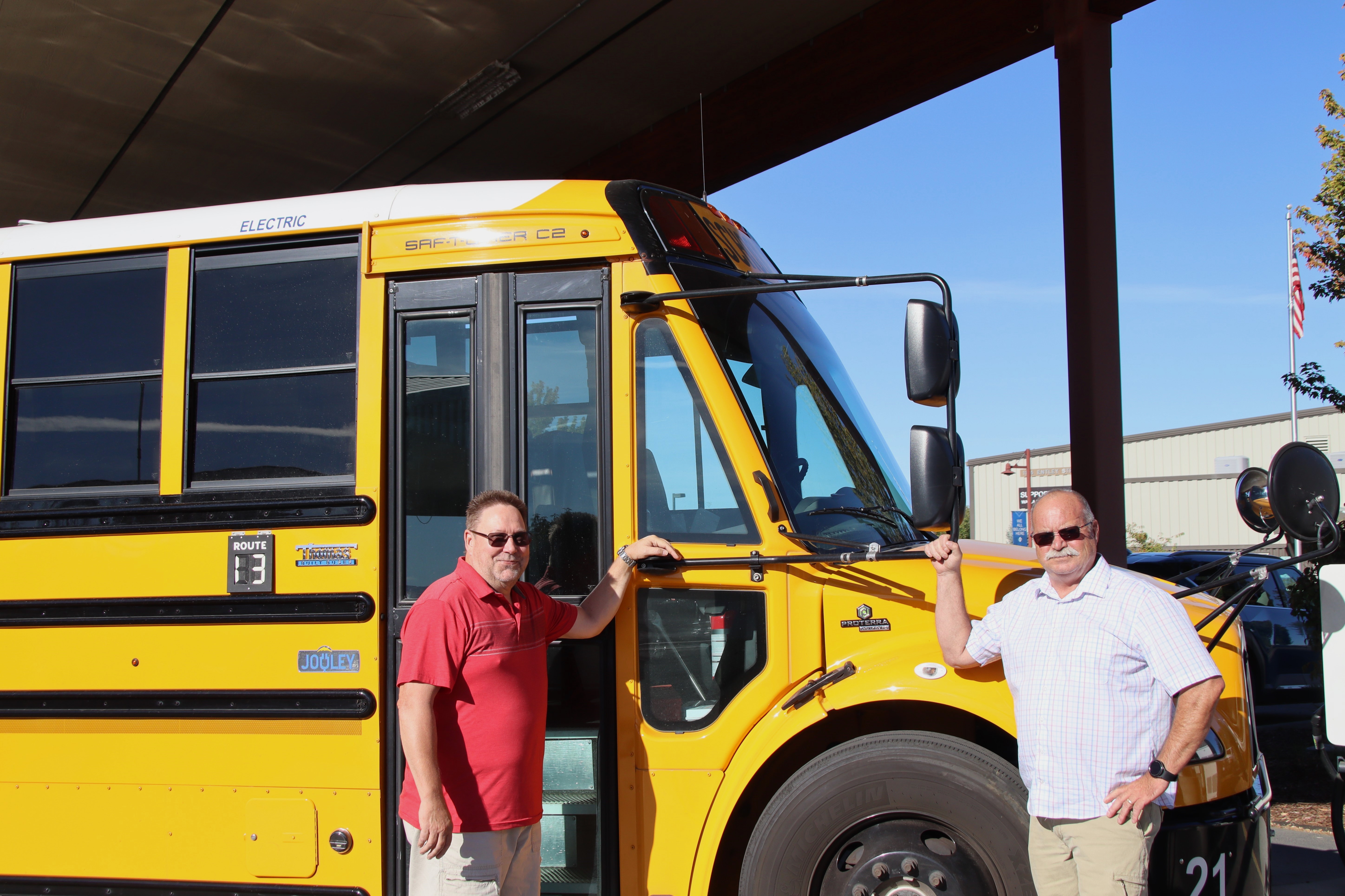 Two people standing next to an electric school bus