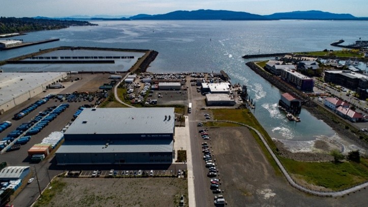 Aerial photo of the Central Waterfront, looking west. Bellingham Bay and the Aeration Stabilization Basin are at the top of the photo. The foreground is of a large paved area with industrial warehouses.