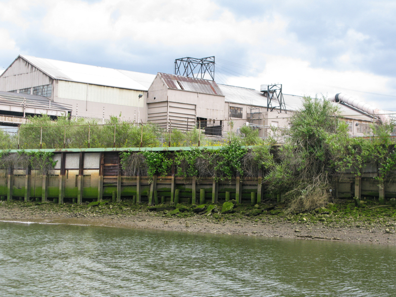 Foreground is a wooden bulkhead along the Duwamish Waterway. Background is a large industrial building. 