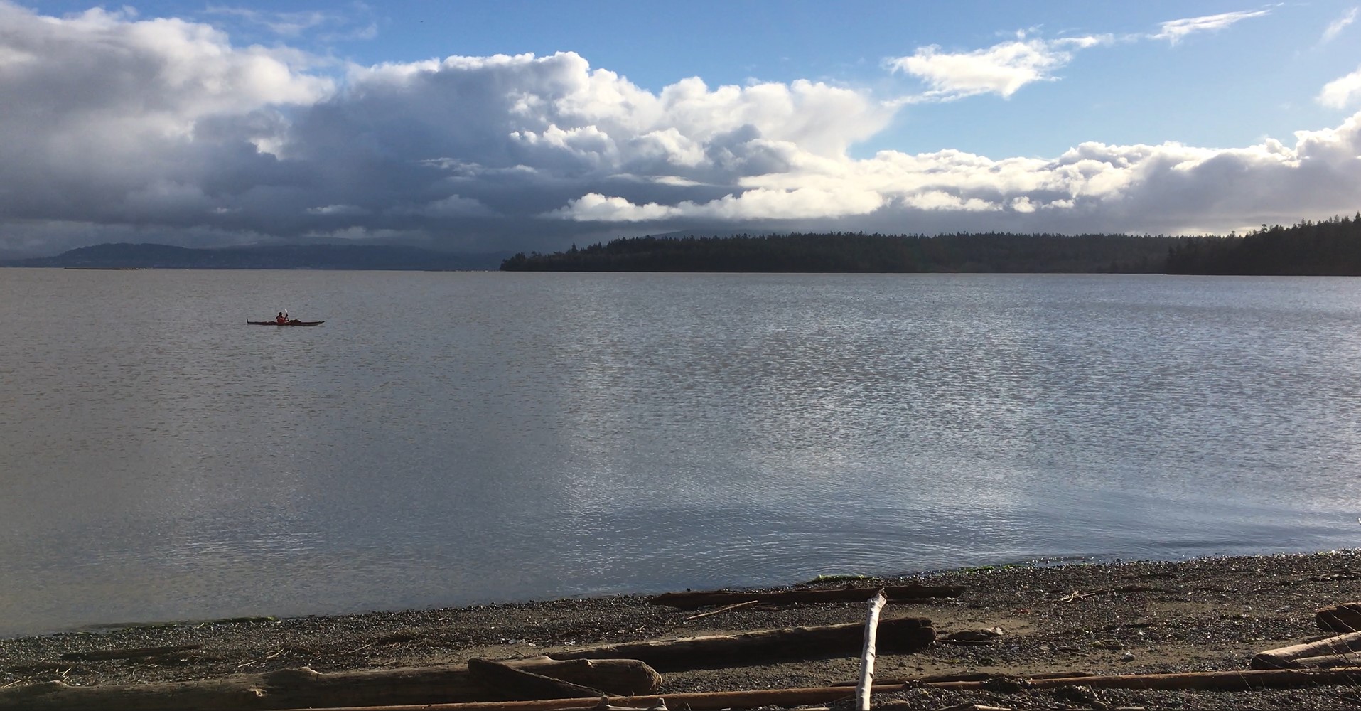 Beach with forested hills in background with kayaker on partly cloudy day