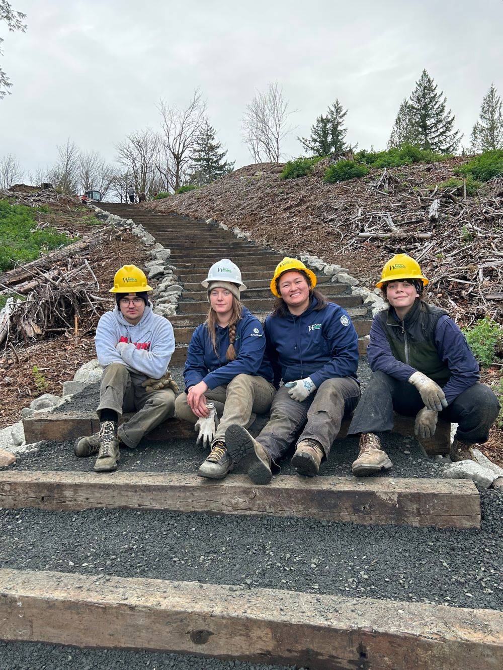 A WCC crew sits on a gravel and wood staircase running through an open restoration site.