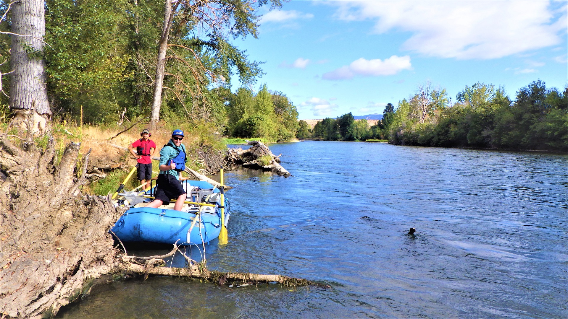 Two people in a raft on the side of a wide river