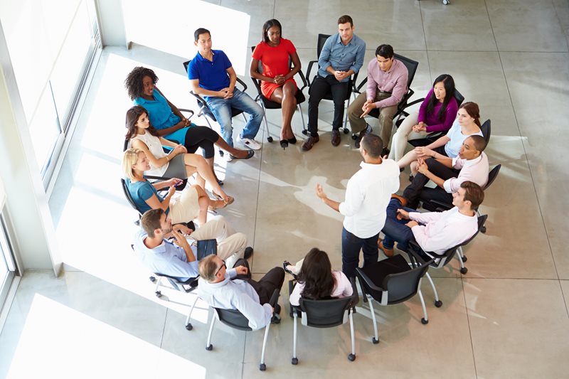 Group of people sitting a circle listening to a speaker.