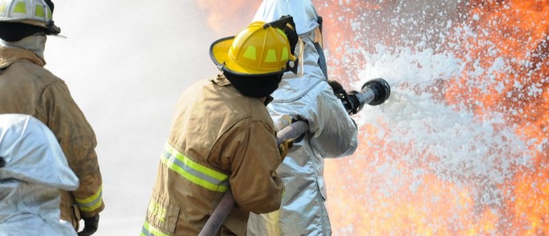 Firefighters spraying firefighting foam toward open flames