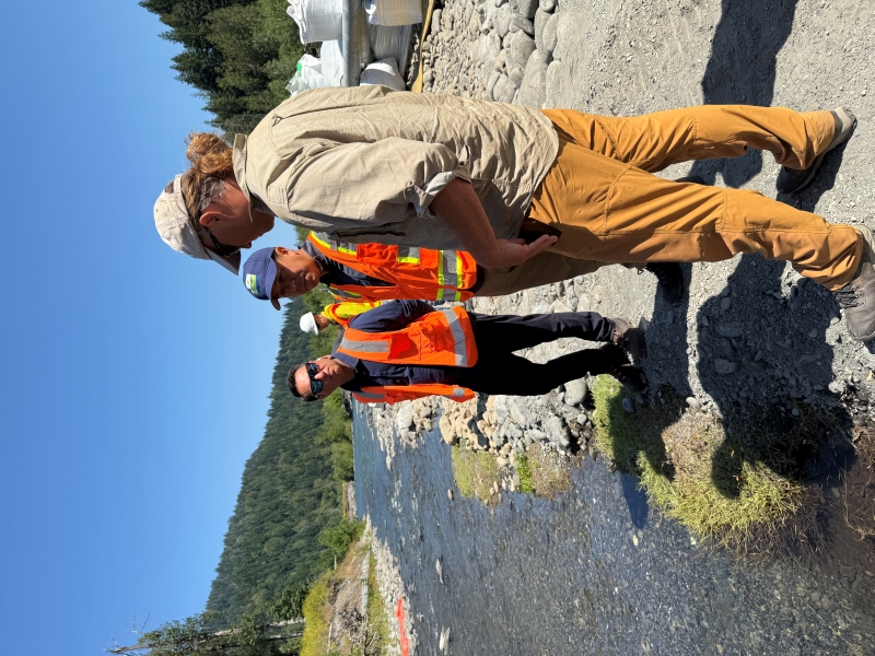Tribal representatives and an Ecology worker stand at the bank of Indian Creek in orange vests and hard hats.