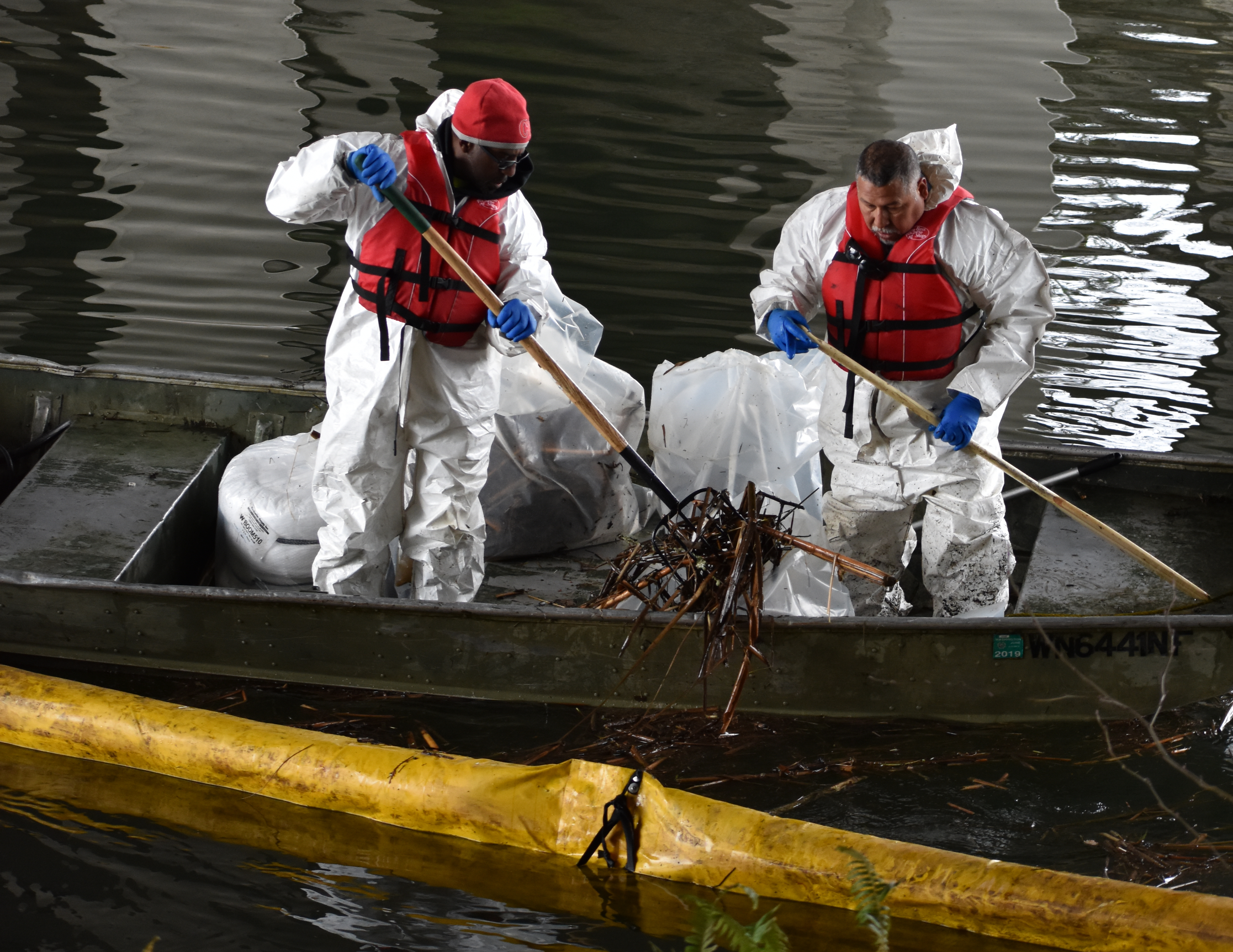 Spill response workers collecting oiled debris out of a lake.