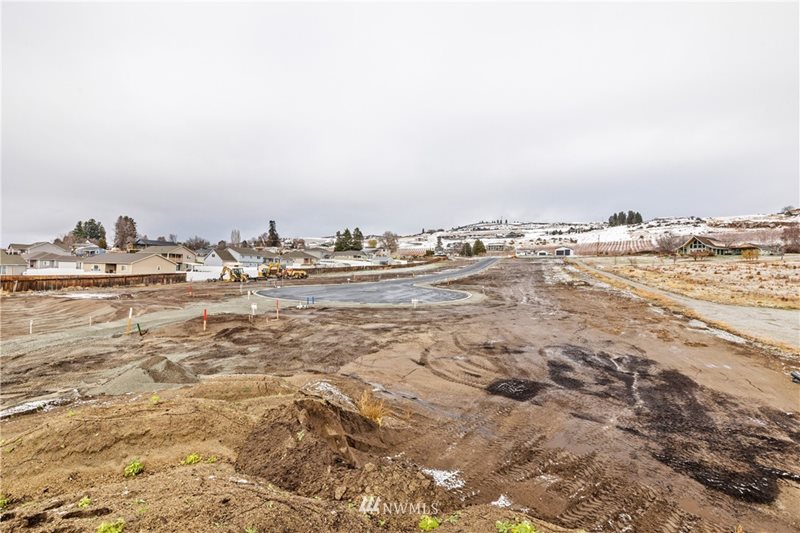 A housing development lot is seen in early stages with earth and soil scraped and mounded in the foreground of a cul-de-sac on a single lot