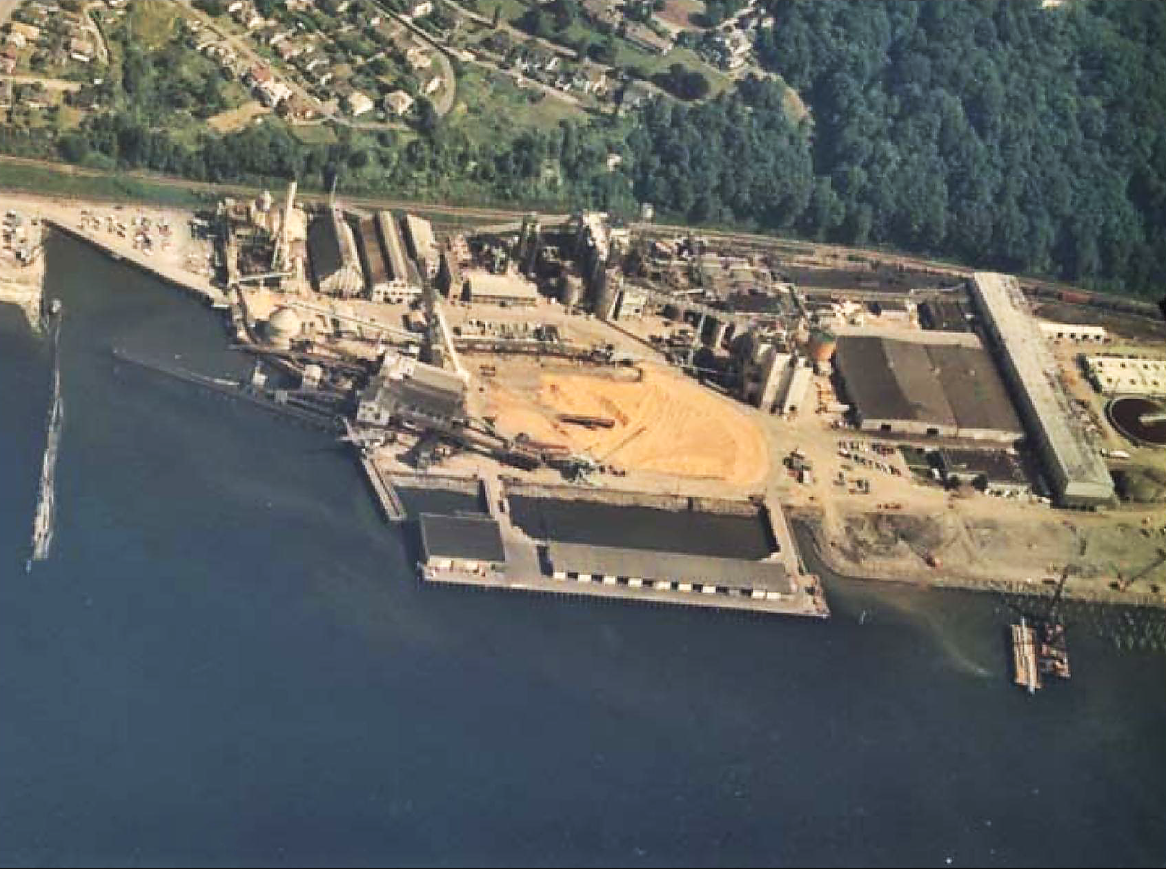 Old photograph of a water-front industrial complex, with warehouses, piers, tanks, smokestacks, and conveyers.