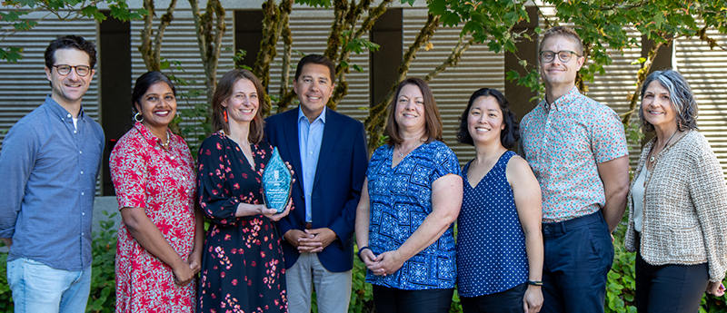 Eight Ecology employees, including Ecology Director Casey Sixkiller gathered to show award statue.