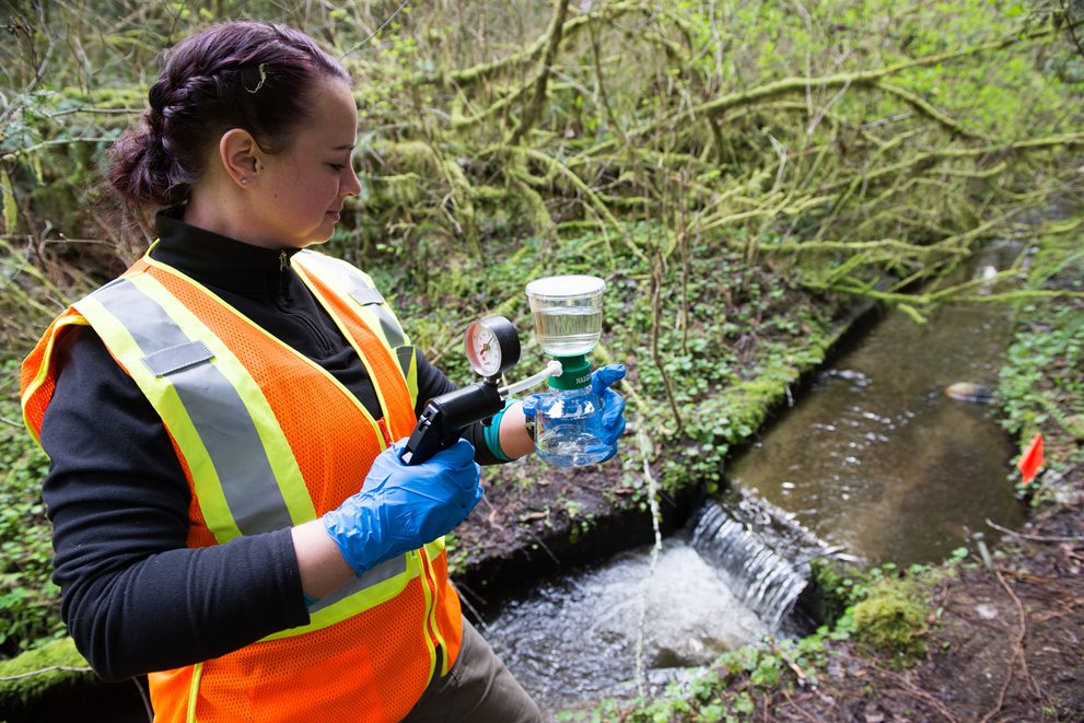 Woman sampling stream water outside.