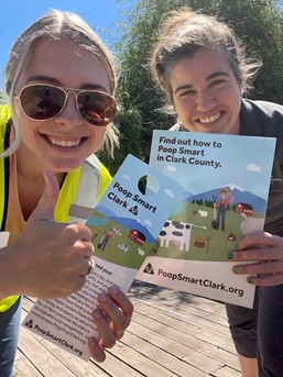 two people smiling at the camera wearing safety gear and holding flyers that say Poop Smart Clark