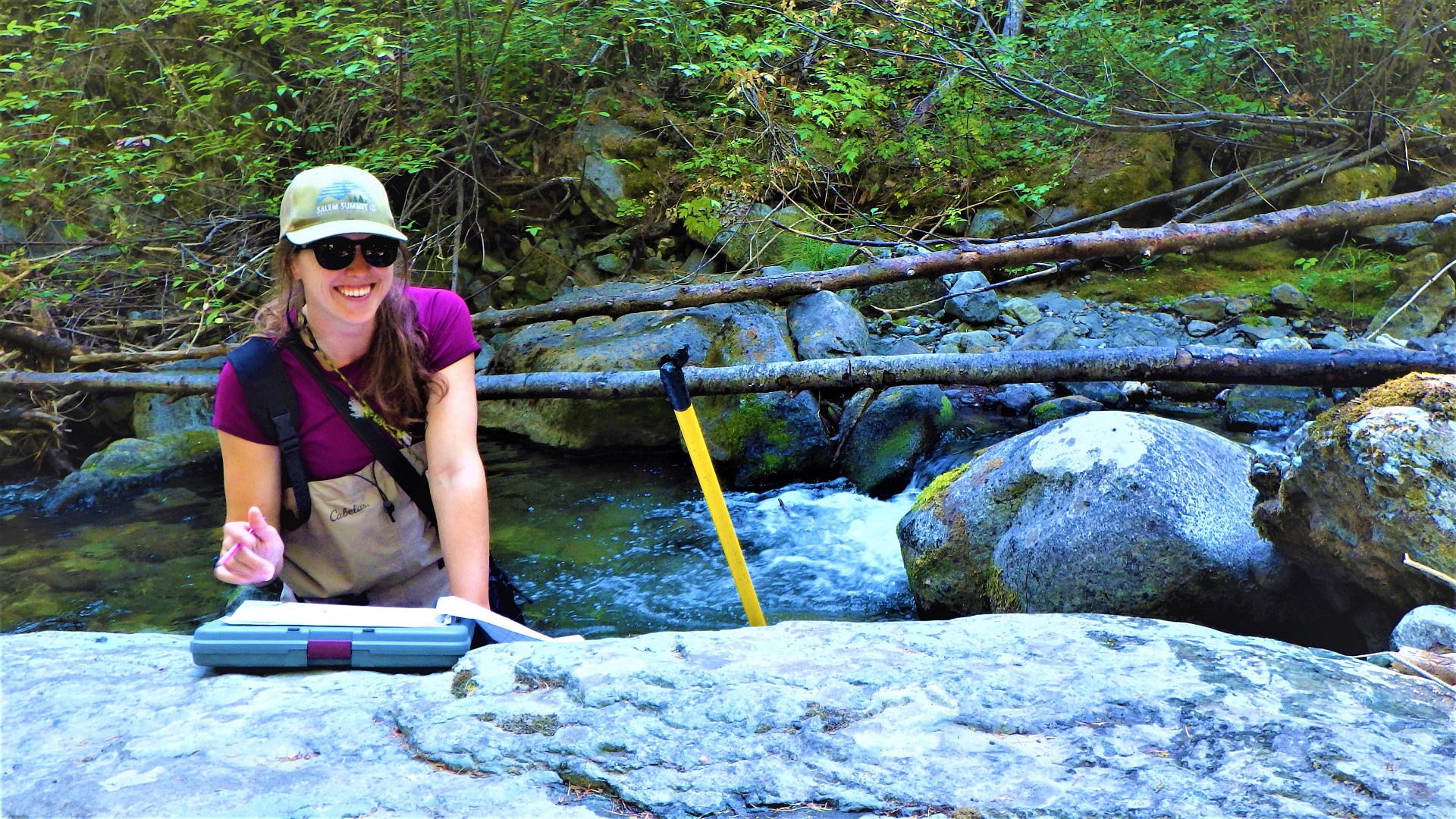 A person leaning on a large boulder while holding a pencil and clipboard