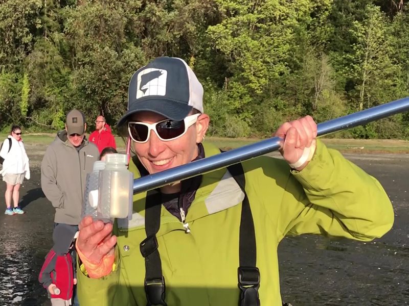 Man in a yellow shirt standing in chest-deep water holding a sampling bottle.