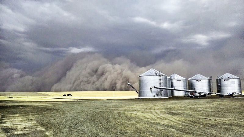 A dust storm approaching silos on a farm field