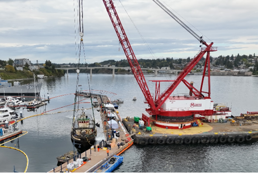 Aerial view of crane, dock with equipment and response personnel, and lifted tug.
