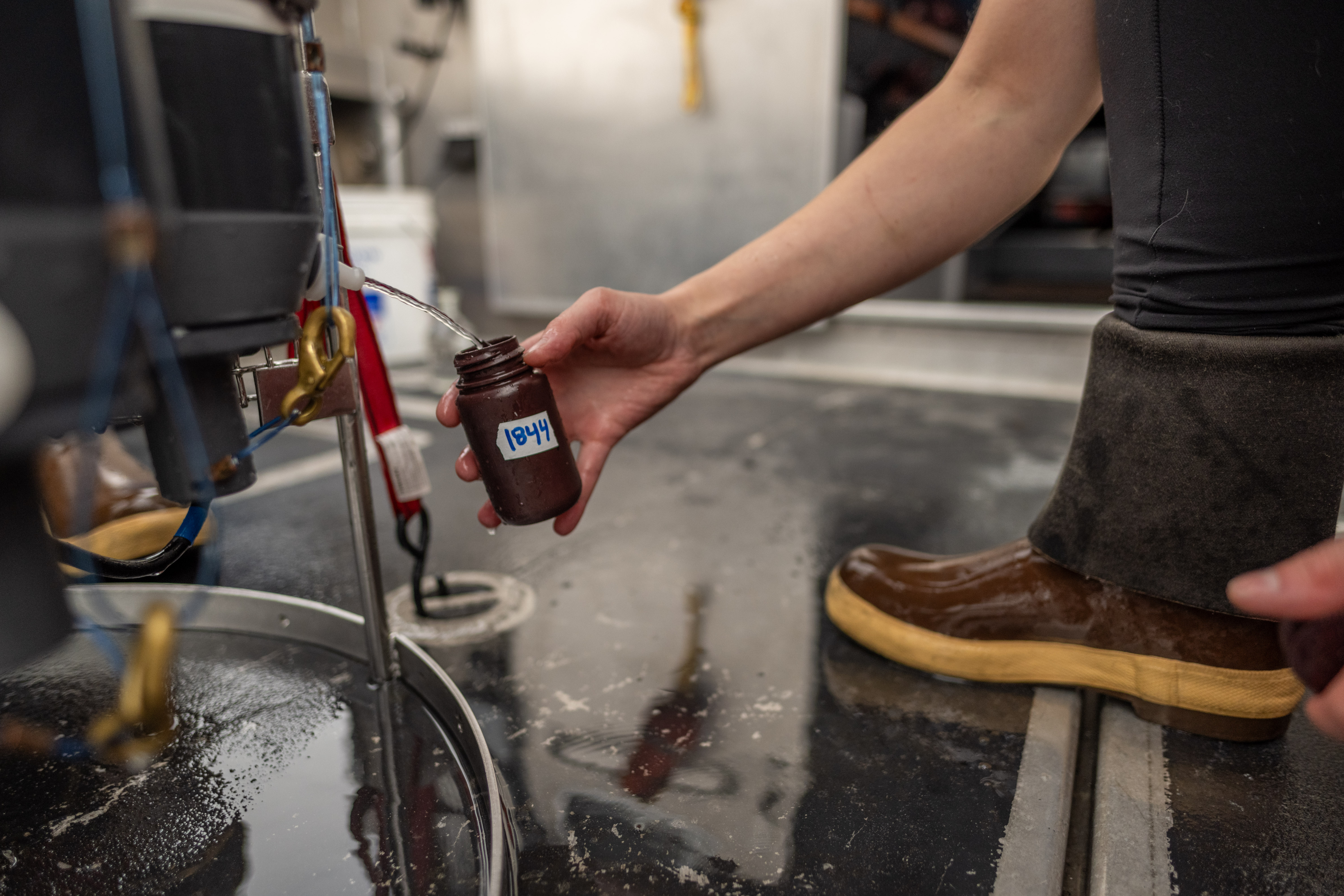 A person collects a sample of seawater as it pours out of a larger container. The water sample will be analyzed in a laboratory.