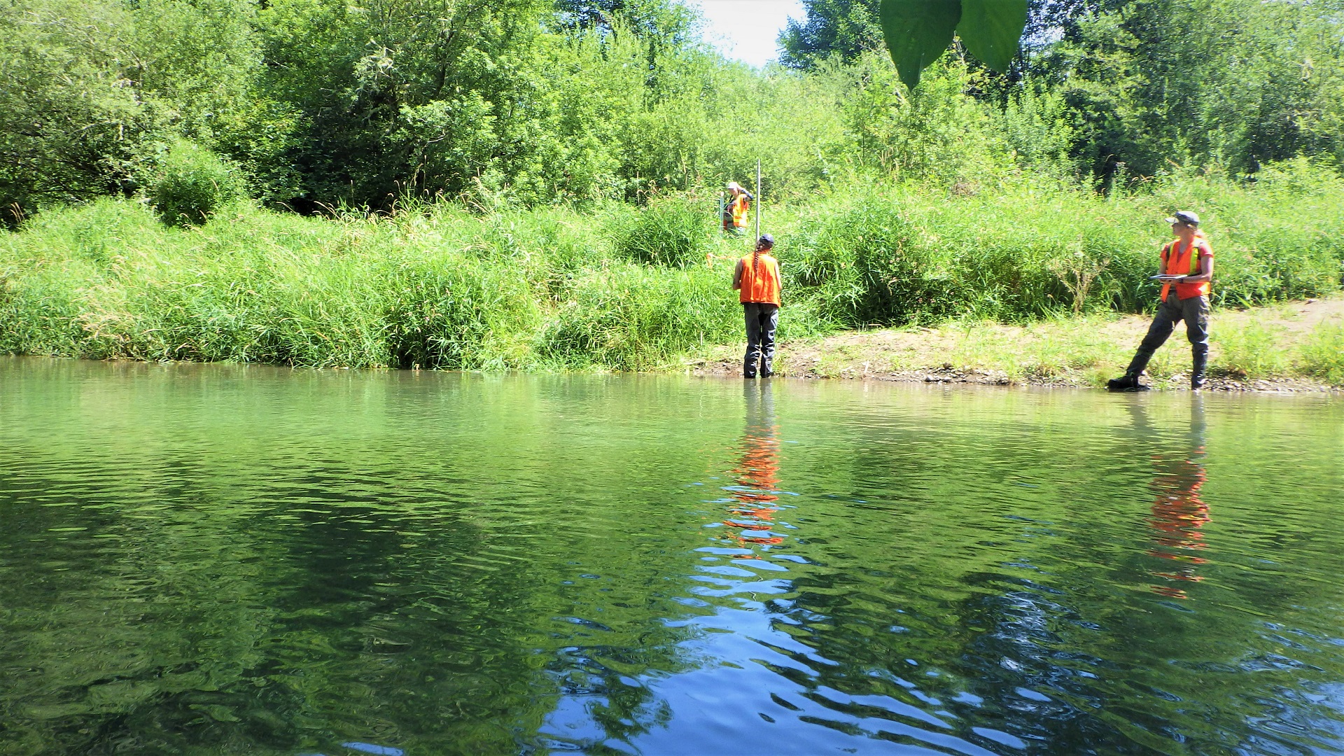 Three crewmembers with measuring rods and clipboards at a large river